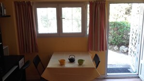 Ein Zimmer mit gedecktem Tisch für zwei Personen, einem Fenster mit Vorhängen und Blick ins Freie.