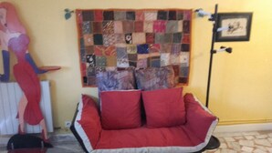 Ein Wohnzimmer mit einem roten Sofa, einer Patchworkdecke und einem gerahmten Bild an der Wand.