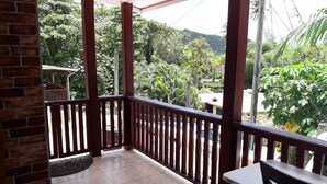 A covered balcony with a tiled floor, wooden railings, and a table with a chair. - Balata Splendour Apartment (Gros Islet)