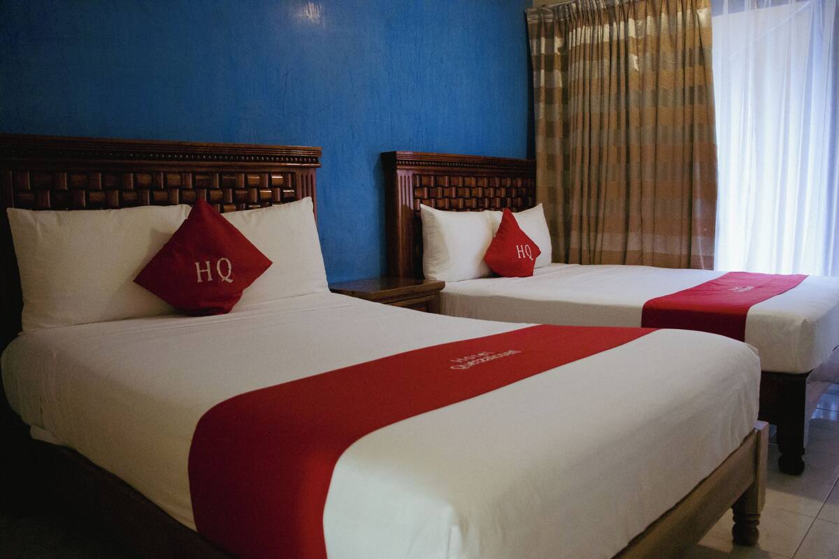 Deux lits doubles avec des têtes de lit en bois, des oreillers rouges et un couvre-lit rouge.