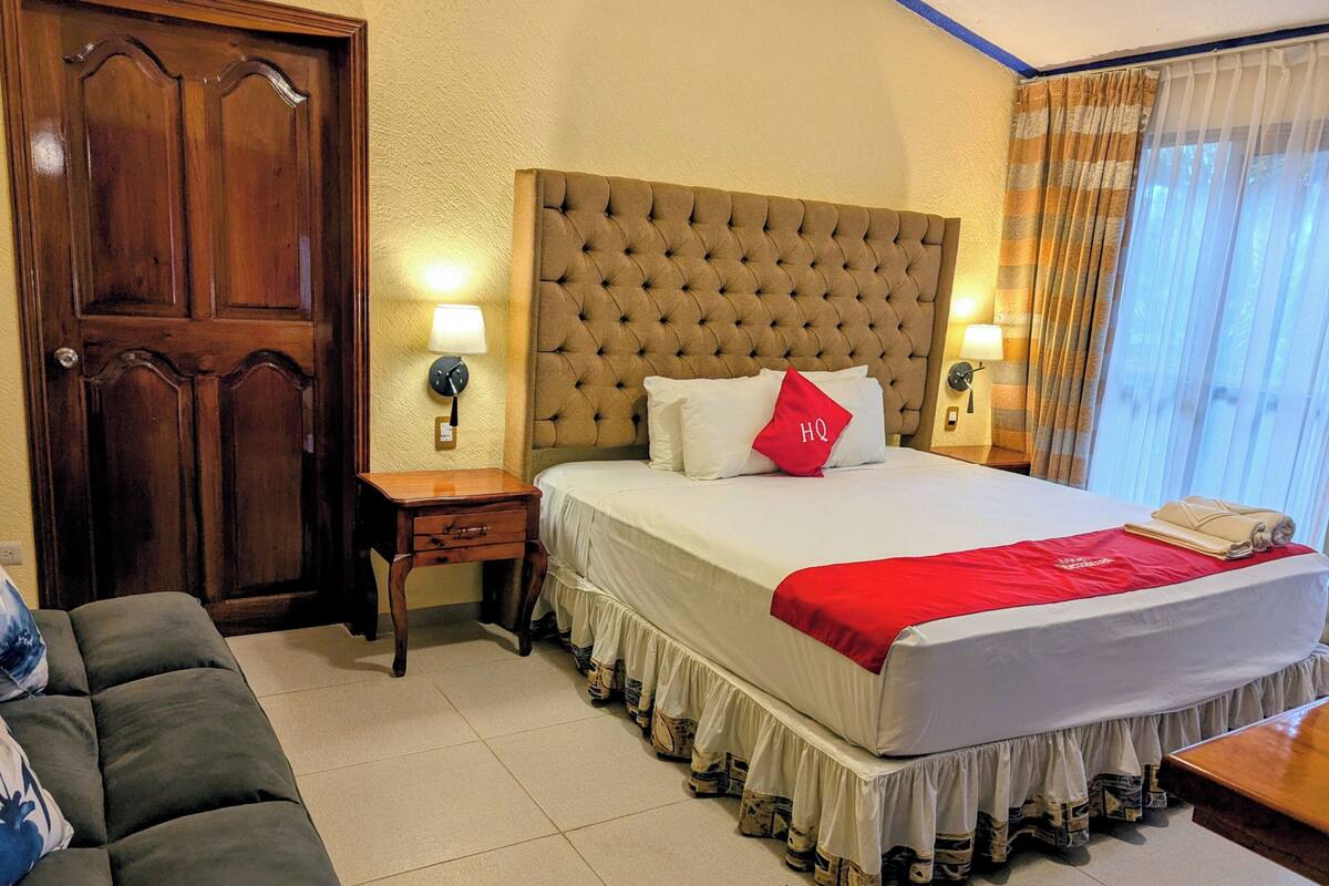 Une chambre d’hôtel avec un grand lit, une porte en bois, une table de chevet avec une lampe et un canapé.