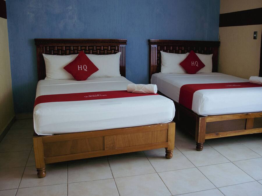 Dos camas de madera con sábanas blancas y almohadas rojas que indican "HQ".