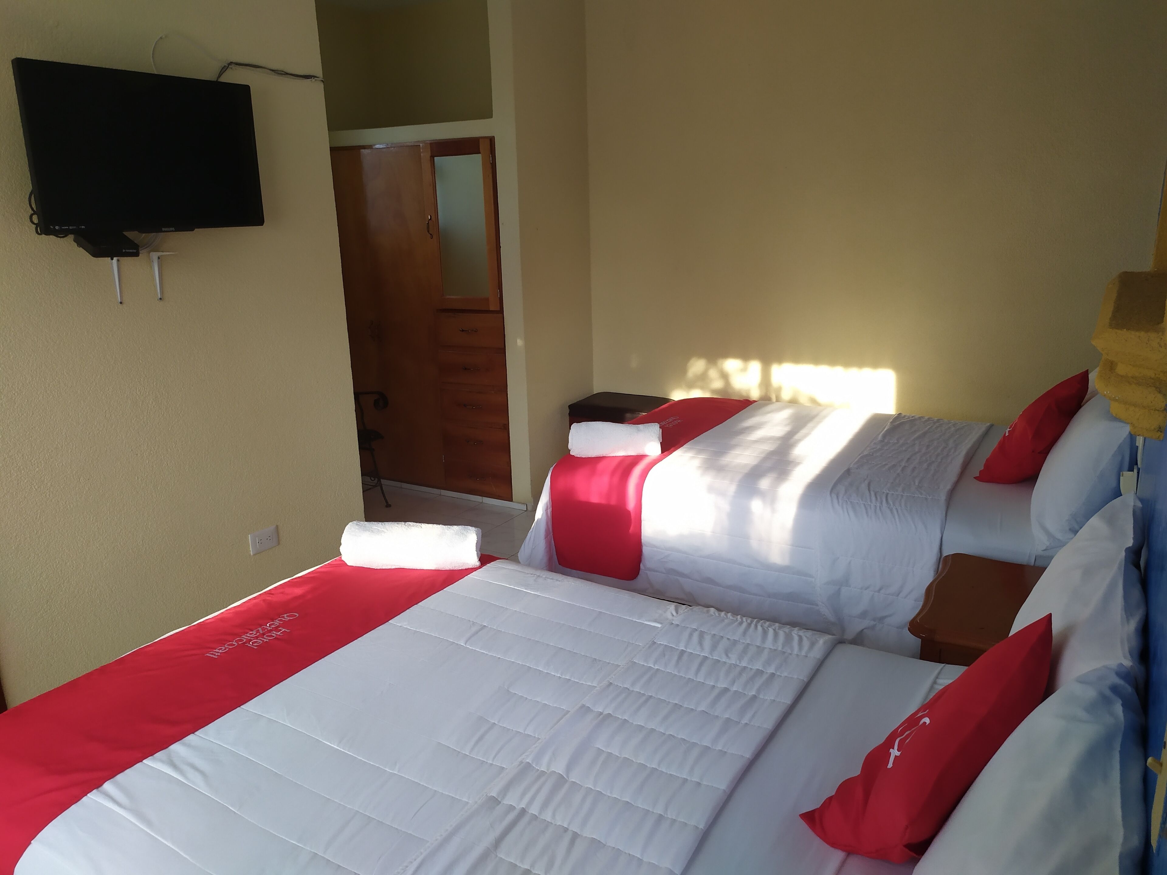 A hotel room with a bed, a TV mounted on the wall, and a wooden door.