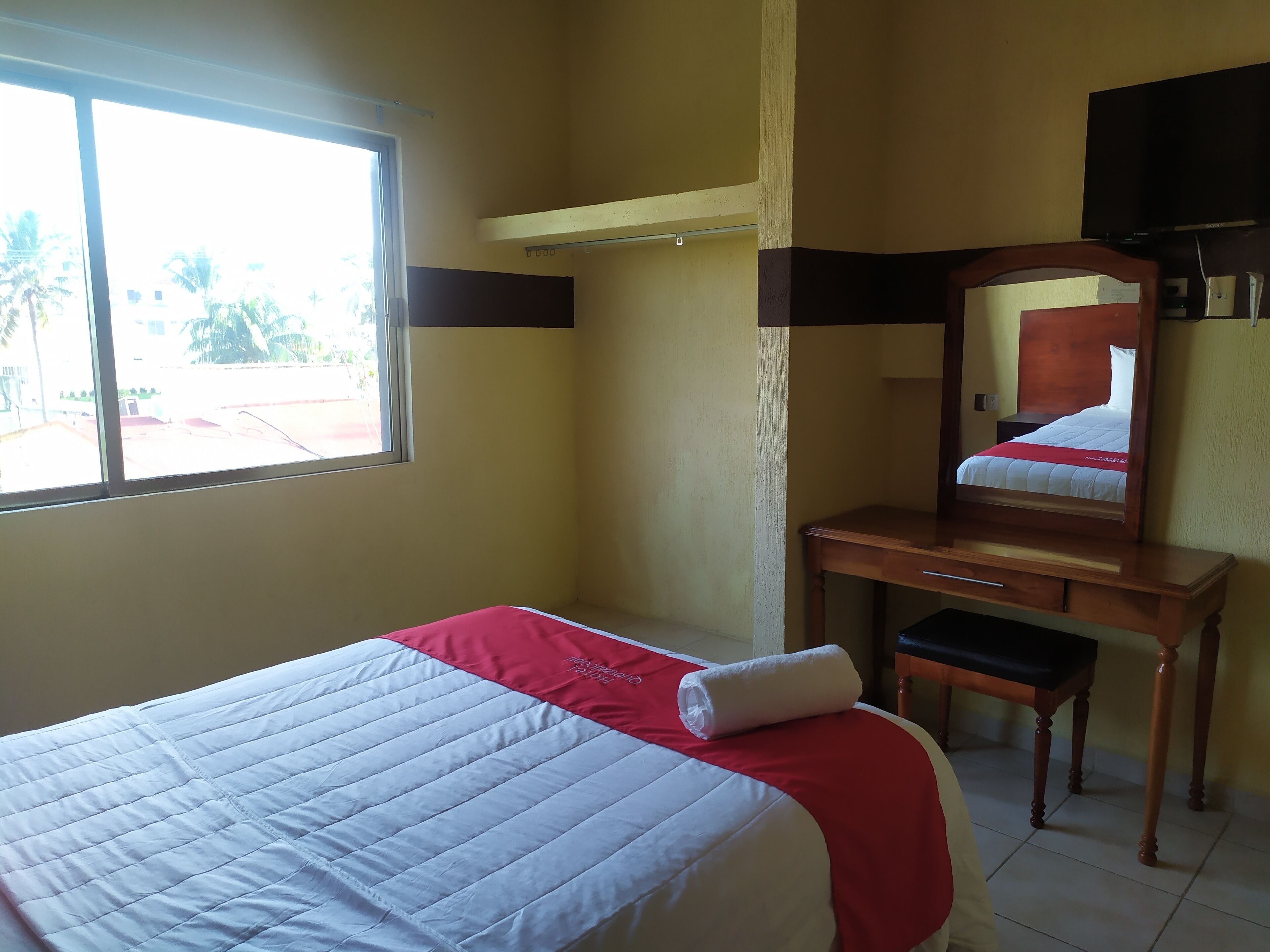 Una habitación de hotel con una cama, un escritorio de madera, un espejo y una ventana.