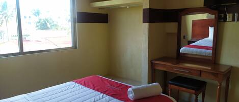 Una habitación de hotel con una cama, un escritorio de madera, un espejo y una ventana.