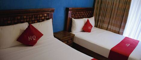 Dos camas de hotel con almohadones y colcha rojos, un cabecero de madera y una mesita de noche.