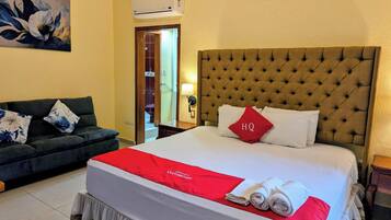 Habitación de hotel con una cama grande, un sofá, un cuadro y un aire acondicionado.