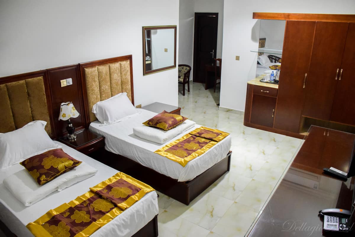 Quarto de hotel com duas camas, uma escrivaninha, uma cadeira, um guarda-roupa e um espelho.