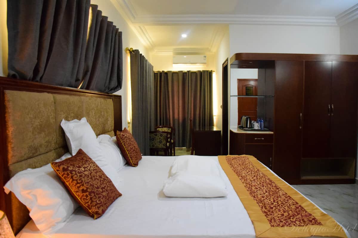 Quarto de hotel com uma cama grande, um guarda-roupa e uma mesa de trabalho com cadeira.