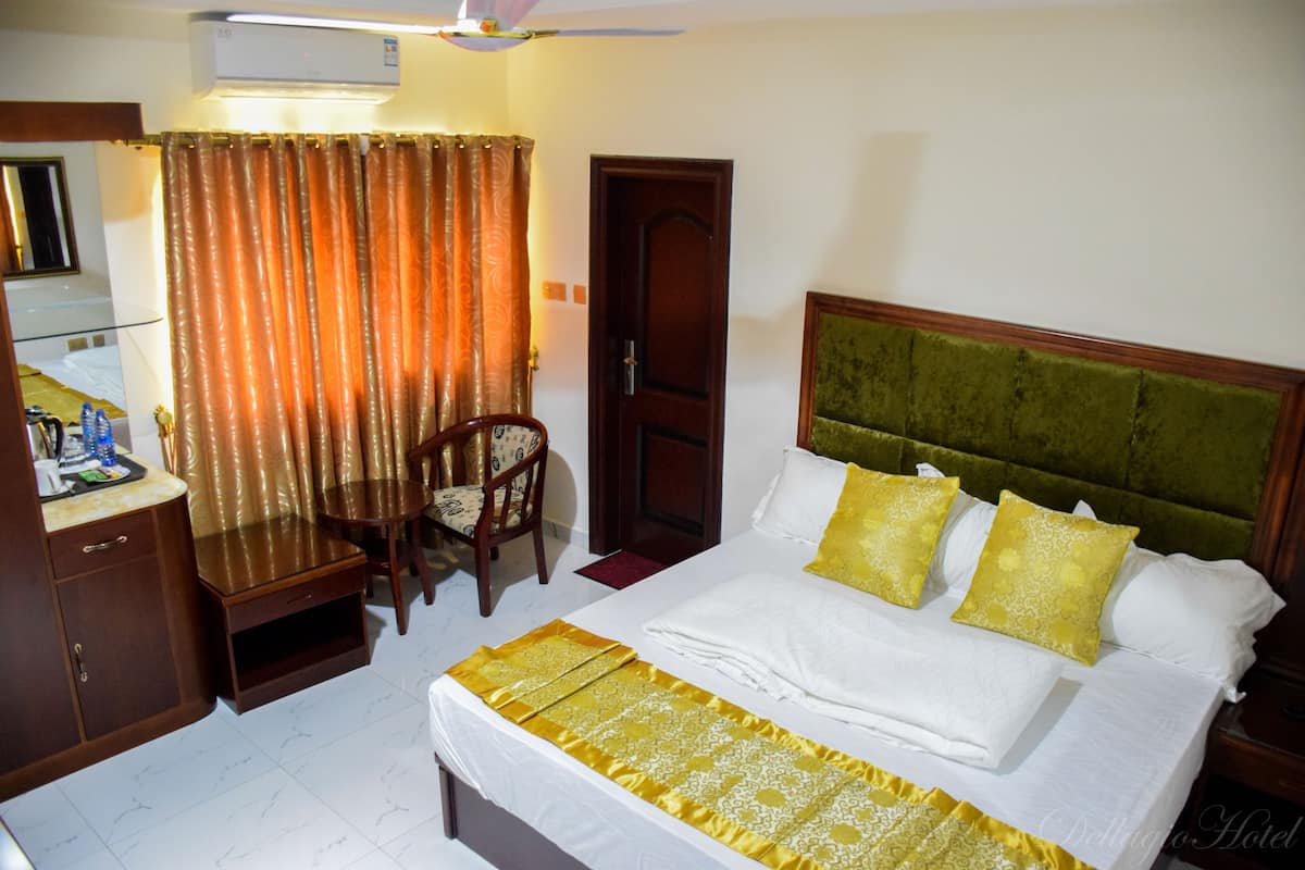 Quarto de hotel com uma cama, escrivaninha, cadeira e guarda-roupa.