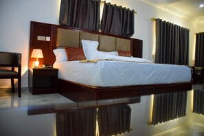 Habitación de hotel con una cama grande, una mesita de noche con lámpara, una silla y un espejo.