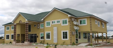 A two-story building with a green roof, multiple windows, and a covered entrance area.