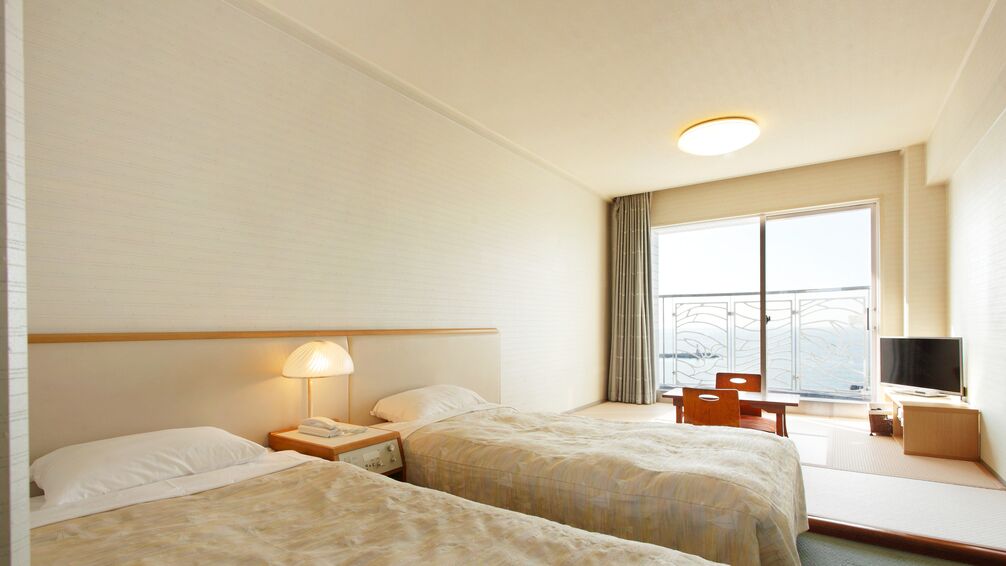 Hotellihuone, jossa on kaksi sänkyä, televisio, työpöytä ja ikkuna, josta on näkymä.