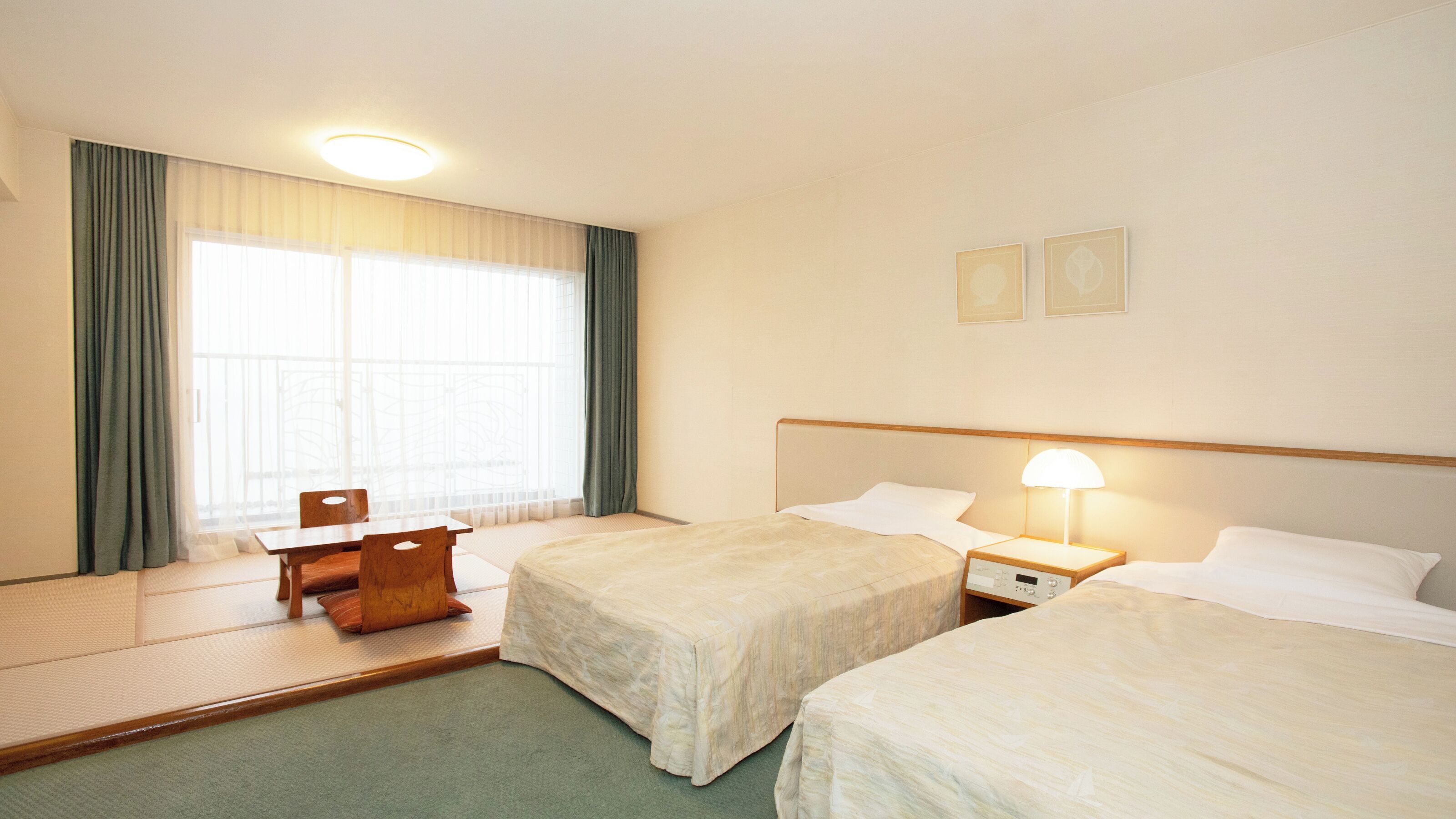 Hotellihuone, jossa on kaksi sänkyä, työpöytä, tuoli, yöpöytä lampun kanssa ja ikkuna, jossa on verhot.