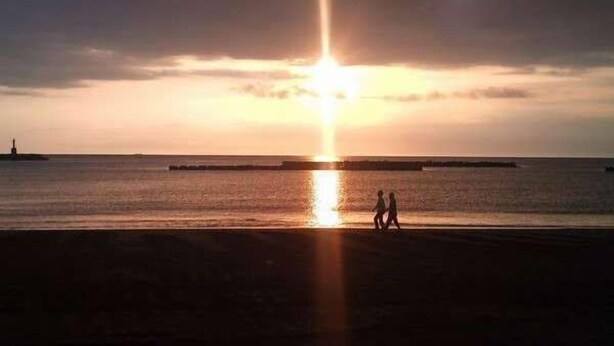 Un coucher de soleil sur une mer calme, avec une jetée visible au loin.