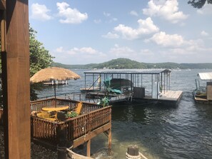 A wooden dock with a thatched roof structure, a covered seating area, and a view of the water and distant hills. - Cozy Vacation Getaway. (Gravois Mills)