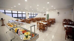 A spacious dining area with multiple tables and chairs, a buffet with various food items, and large windows offering a view.