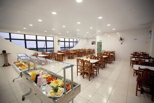 Un comedor amplio con varias mesas y sillas, un bufé con diferentes opciones de comida y grandes ventanales con vistas.