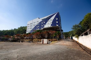 A modern building with a unique angular design, surrounded by a gravel area and trees. - Hotel Caminho do Rosário (Aparecida)