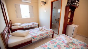 A hotel room with two single beds, a small bathroom, a wooden wardrobe, and a TV mounted on the wall.