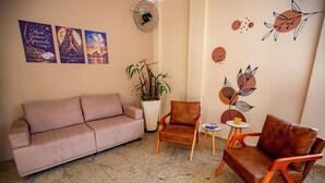 A living room with a sofa, two chairs, a small table, a potted plant, wall art, and a fan.