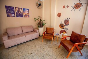 Una sala de estar con un sofá, dos sillones, una mesita, una planta en maceta, adornos en la pared y un ventilador.