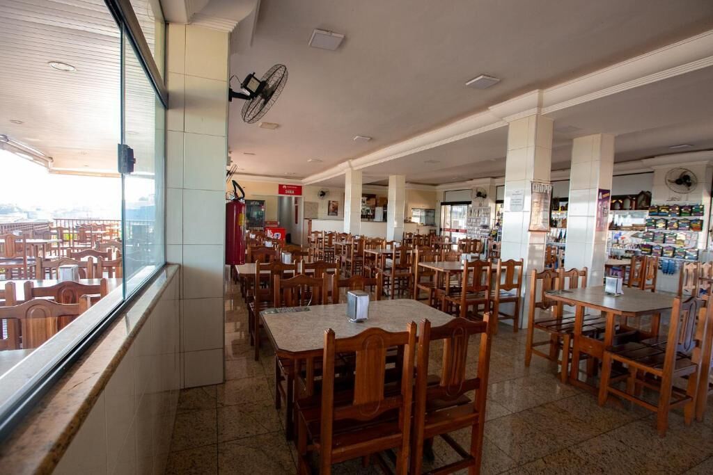 Un restaurante espacioso con varias mesas y sillas de madera, un ventanal con vistas y un ventilador en el techo.