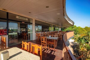 Un área de comedor al aire libre con mesas y sillas de madera, un escaparate de vidrio y vistas a la vegetación.