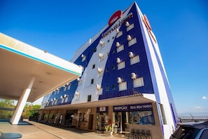 A hotel with a blue and white facade, a reception area, and a visible sign for 'SEJA BEM VINDO'.
