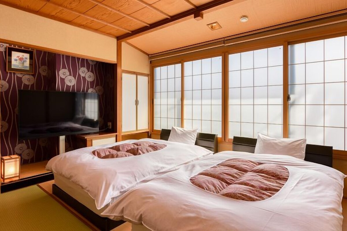 A traditional Japanese-style bedroom with tatami flooring, a futon bed, sliding shoji doors, and a television.