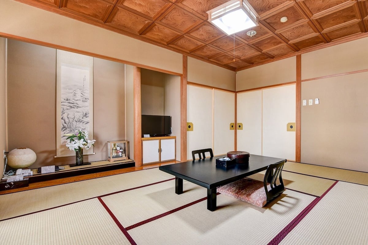 Ein traditioneller japanischer Raum mit Tatami-Bodenbelag, einem niedrigen Tisch, einem Fernseher und einer Schiebetür.