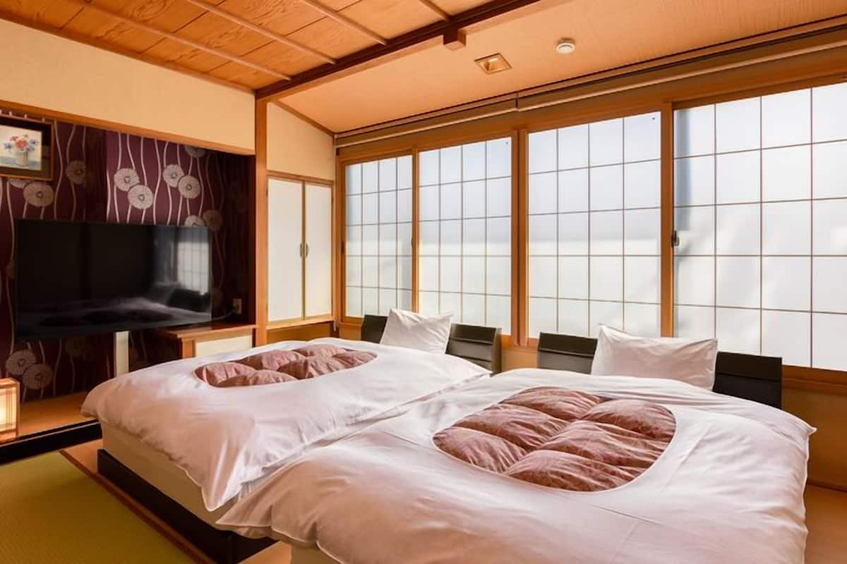 Ein traditionelles japanisches Schlafzimmer mit Tatami-Böden, einem Futonbett, verschiebbaren Shoji-Türen und einem Fernseher.
