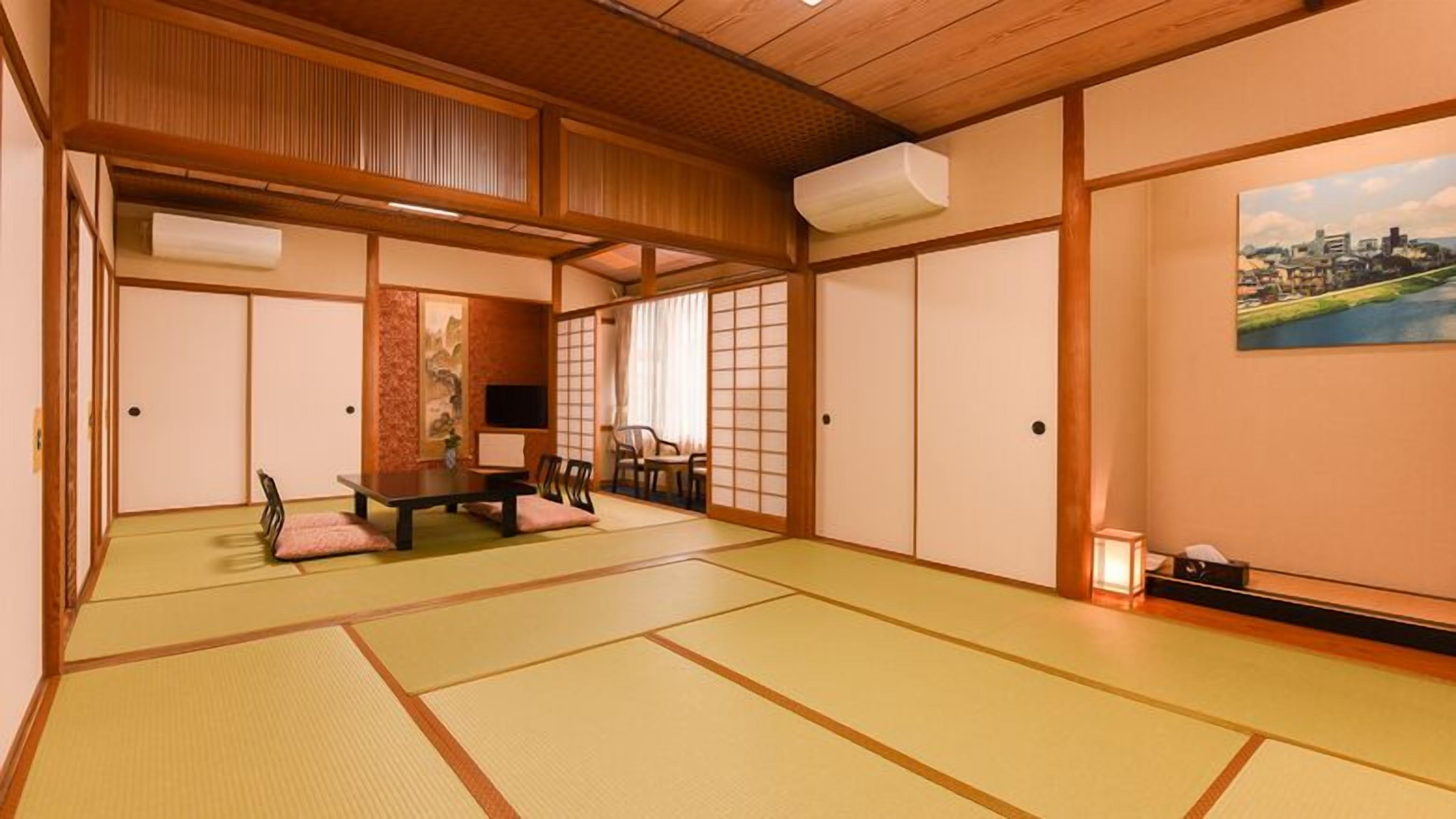 Estada tradicional japonesa amb sòl de tatami, una taula baixa amb coixins, portes corredisses i una pintura d'un paisatge urbà.