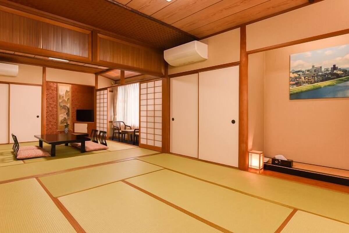 Ein traditioneller japanischer Raum mit Tatami-Böden, einem niedrigen Tisch mit Kissen, Schiebetüren und einem Stadtbild.