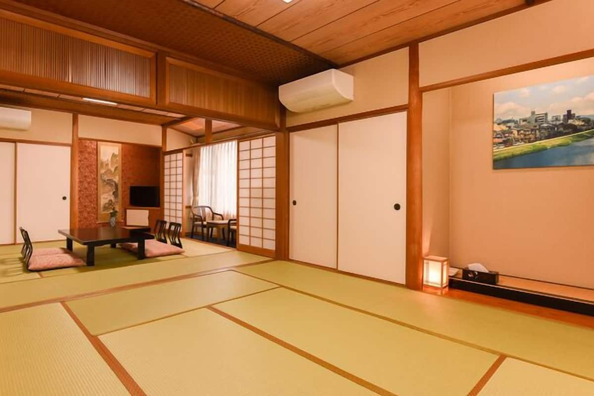 Una habitación japonesa tradicional con suelo de tatami, una mesa baja con cojines, puertas correderas y un cuadro de un paisaje urbano.