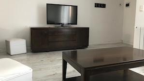 A modern living room with a dark wooden cabinet, a flat-screen TV, and a white ottoman.