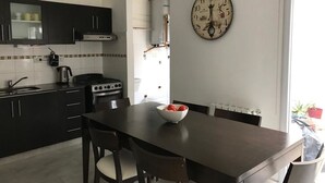 A modern kitchen with dark cabinetry, a stove, and a dining table with chairs. A large wall clock is visible.