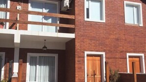 A two-story brick house with a balcony, a wooden door, and a small garden area.