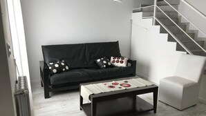 A modern living room with a black sofa, a white ottoman, and a coffee table with a patterned tray. A staircase is visible in the background.