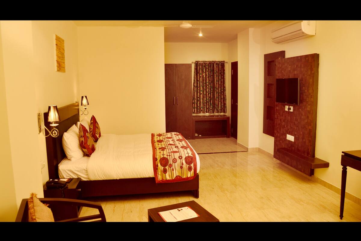 A hotel room with a bed, bedside table, lamp, and a television mounted on the wall.