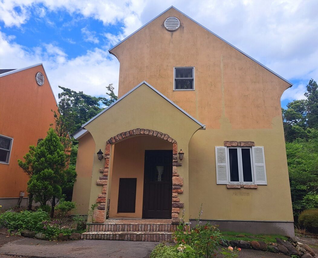 A two-story house with a stone archway entrance, a small window, and a door.