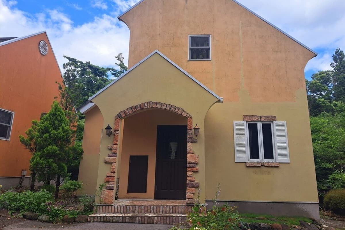A two-story house with a stone archway entrance, a small window, and a door.