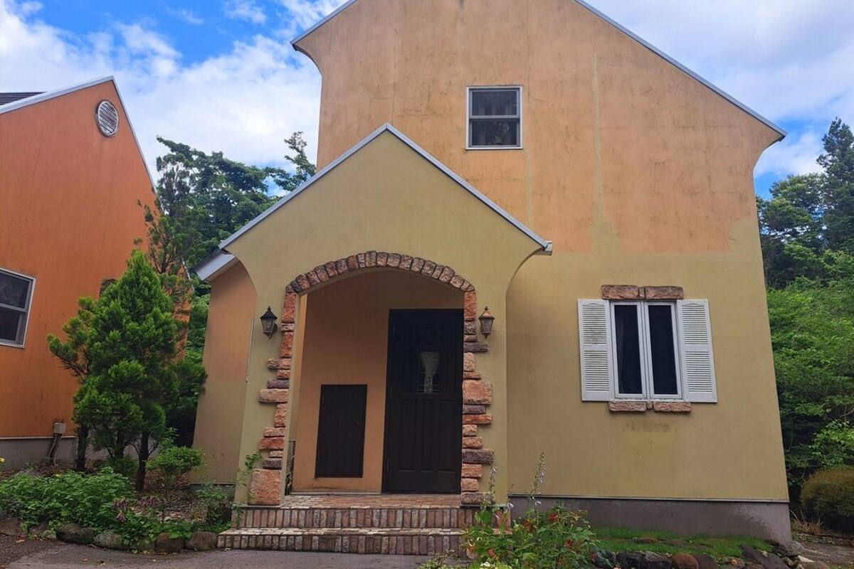 A two-story house with a stone archway entrance, a small window, and a door.