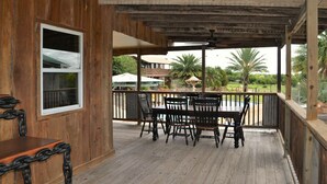 Terraza de madera con mesa y sillas, con vistas a una piscina y palmeras.
