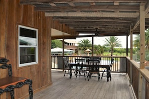 A wooden deck with a table and chairs, overlooking a pool and palm trees. - Laguna Vista Tree House, Cloud Lane (New Braunfels)