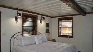 Un dormitorio con una cama, dos lámparas de pared y dos ventanas con persianas.