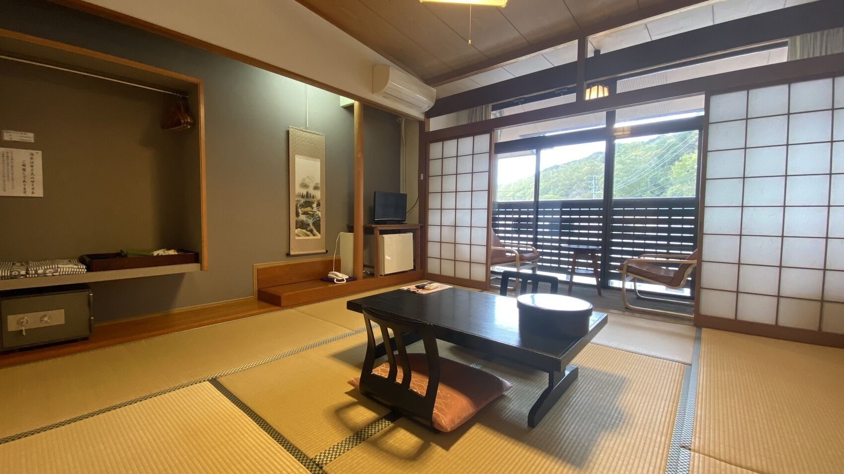 Ein Raum mit Tatami-Matten, einem niedrigen Tisch, einem Fernseher und Blick auf einen Berg durch einen Shoji-Bildschirm.