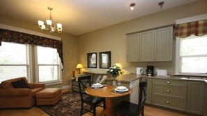 A cozy living room with a wooden dining table, a sofa, and a coffee table. There is a kitchen area with cabinets and a window. - Windmill walk (Dartmouth)