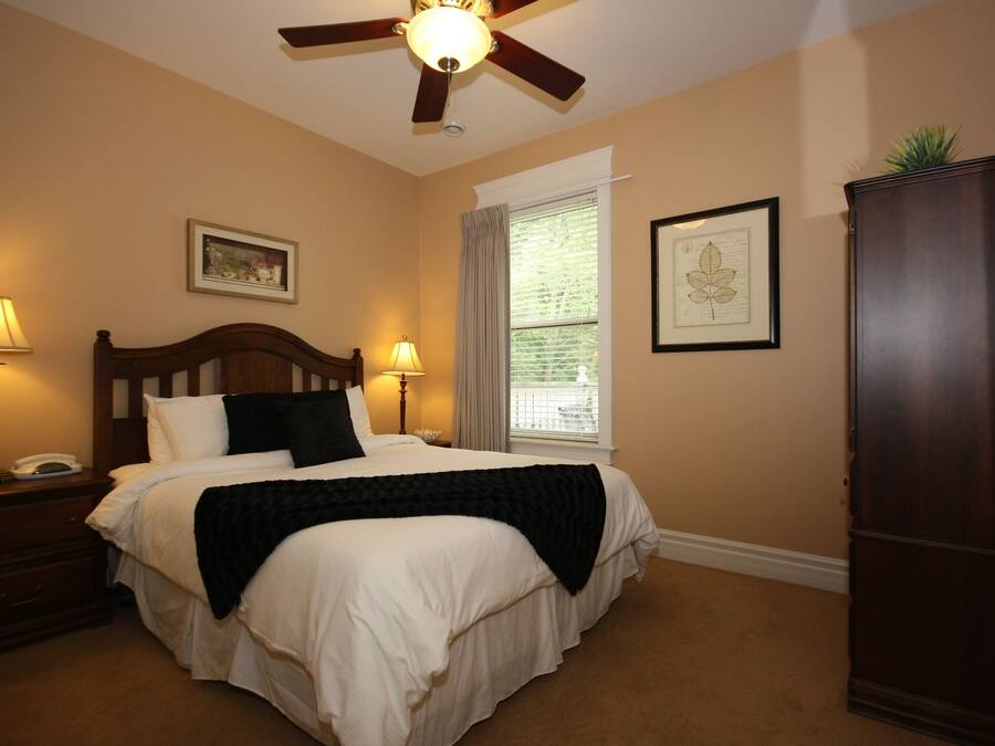 A bedroom with a bed, two bedside lamps, a ceiling fan, a window with blinds, and a wooden cabinet.