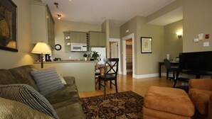A living room with a sofa, a coffee table, and a rug. There is a kitchen area with cabinets and a microwave. A dining table with chairs is visible in the background. - Windmill walk (Dartmouth)